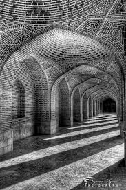 The interior colonnade of a Mithraic temple complex in Nourestan, constructed in the classical style of the late Six Lands period. The repeating arch form reflects Mithraic architectural principles: a progressive movement toward light, with each arch framing the next area as Mehr’s warmth advances through Tārikī.